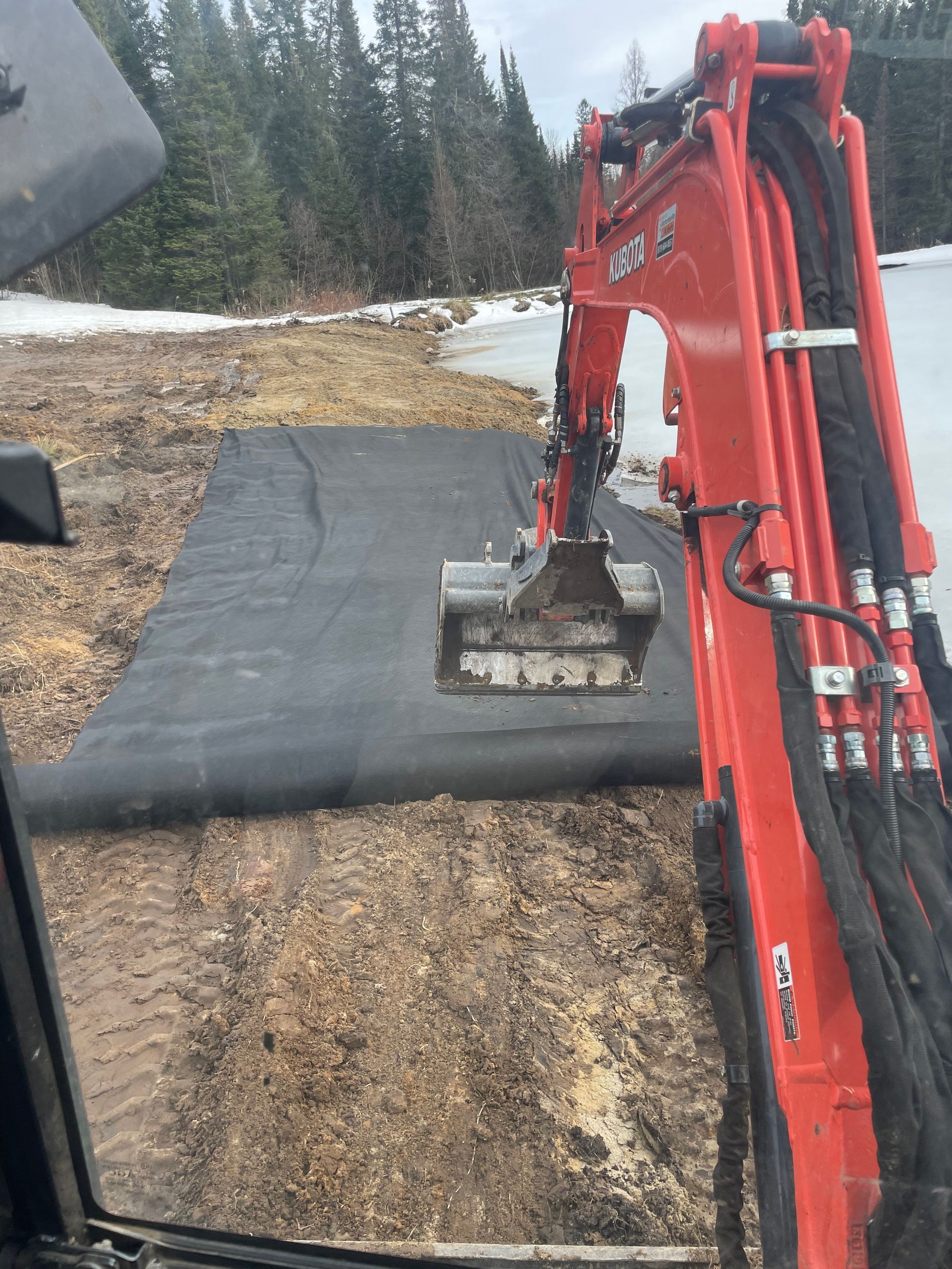 A red excavator is sitting on top of a black mat in the dirt.