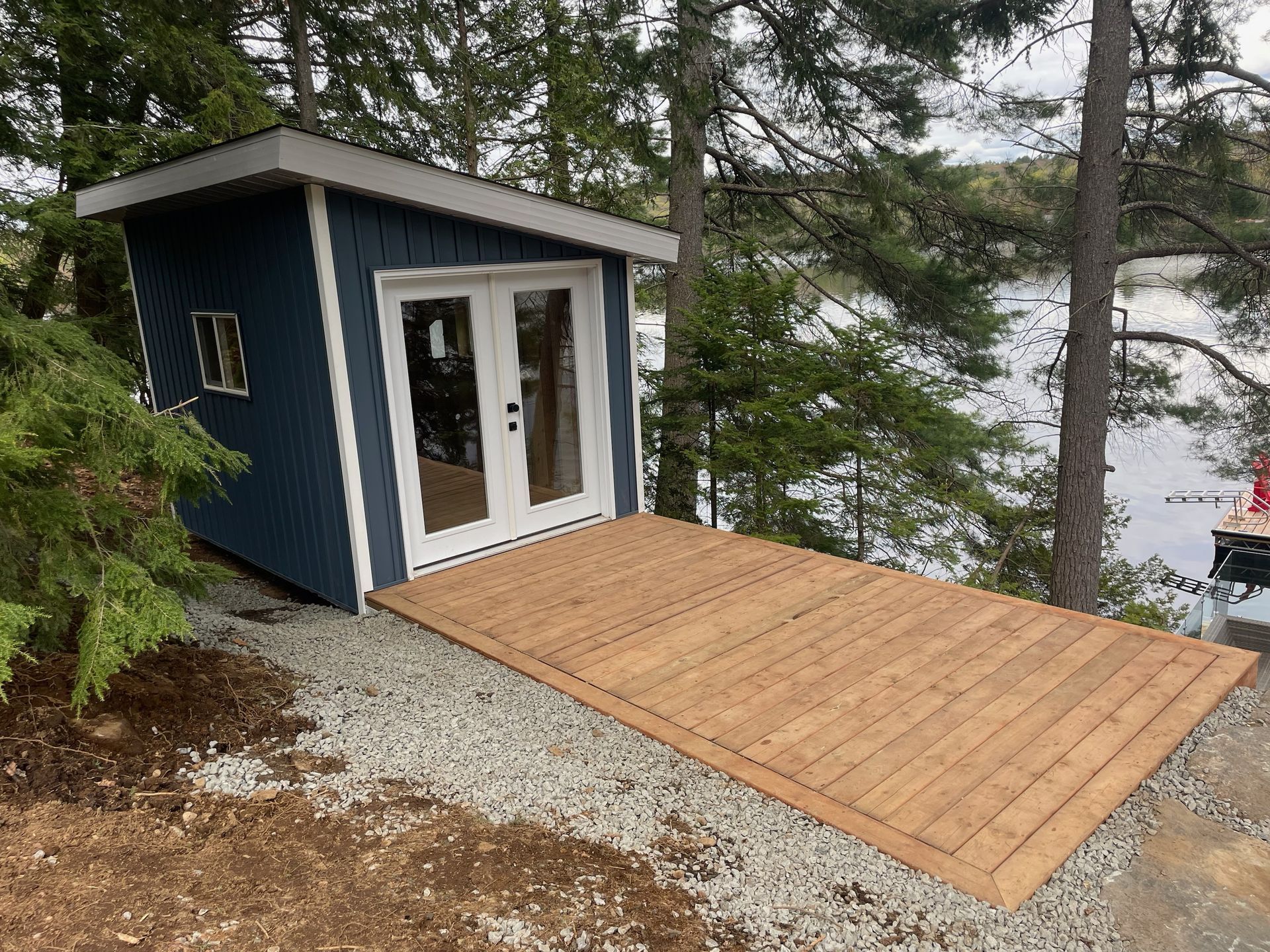 A blue shed with a wooden deck next to a lake.
