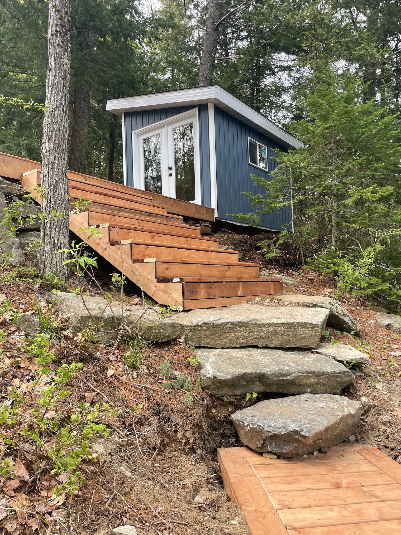 A blue shed is sitting on top of a hill with stairs leading up to it.