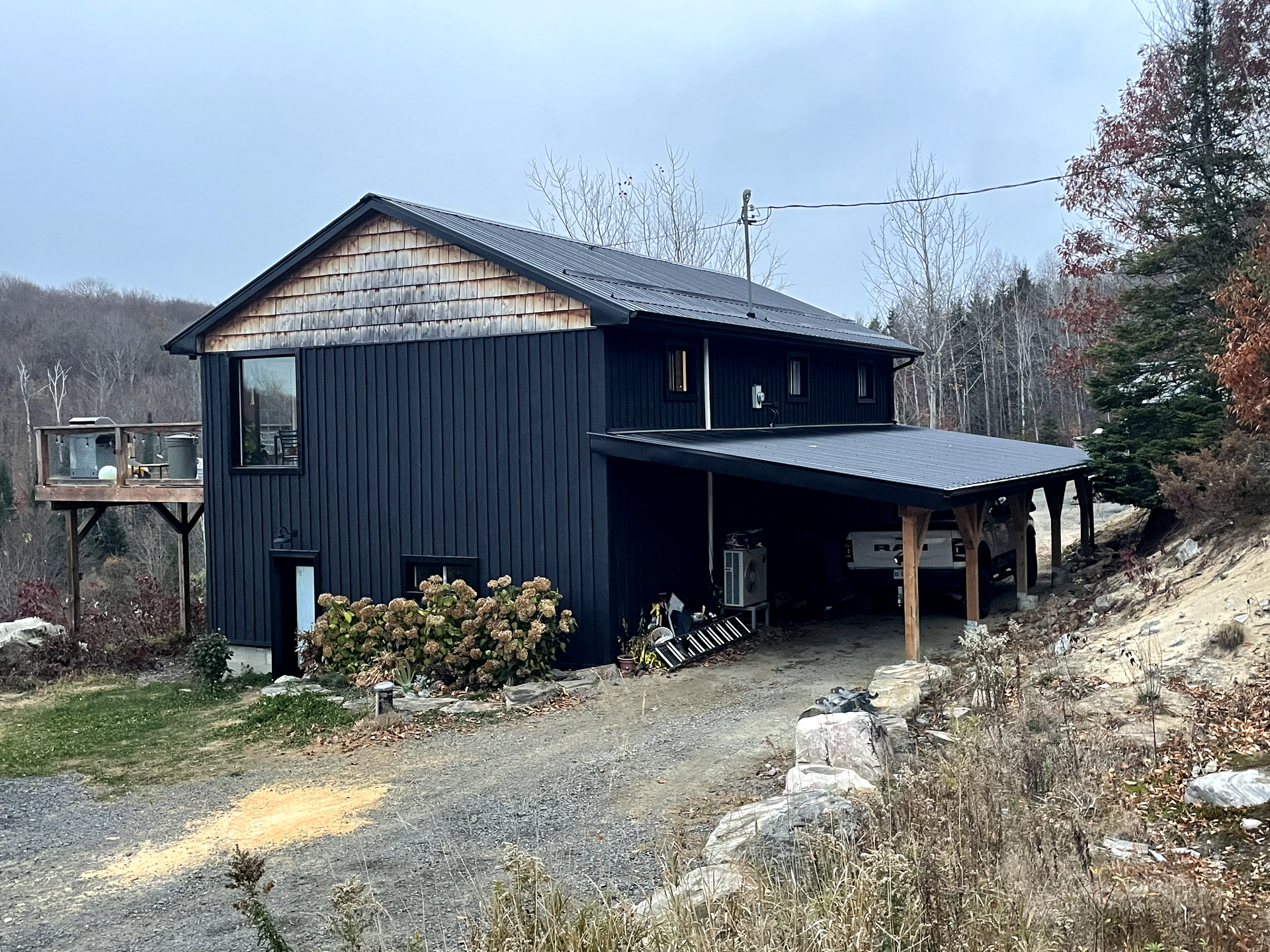 A black house with a carport underneath it is sitting on top of a hill.