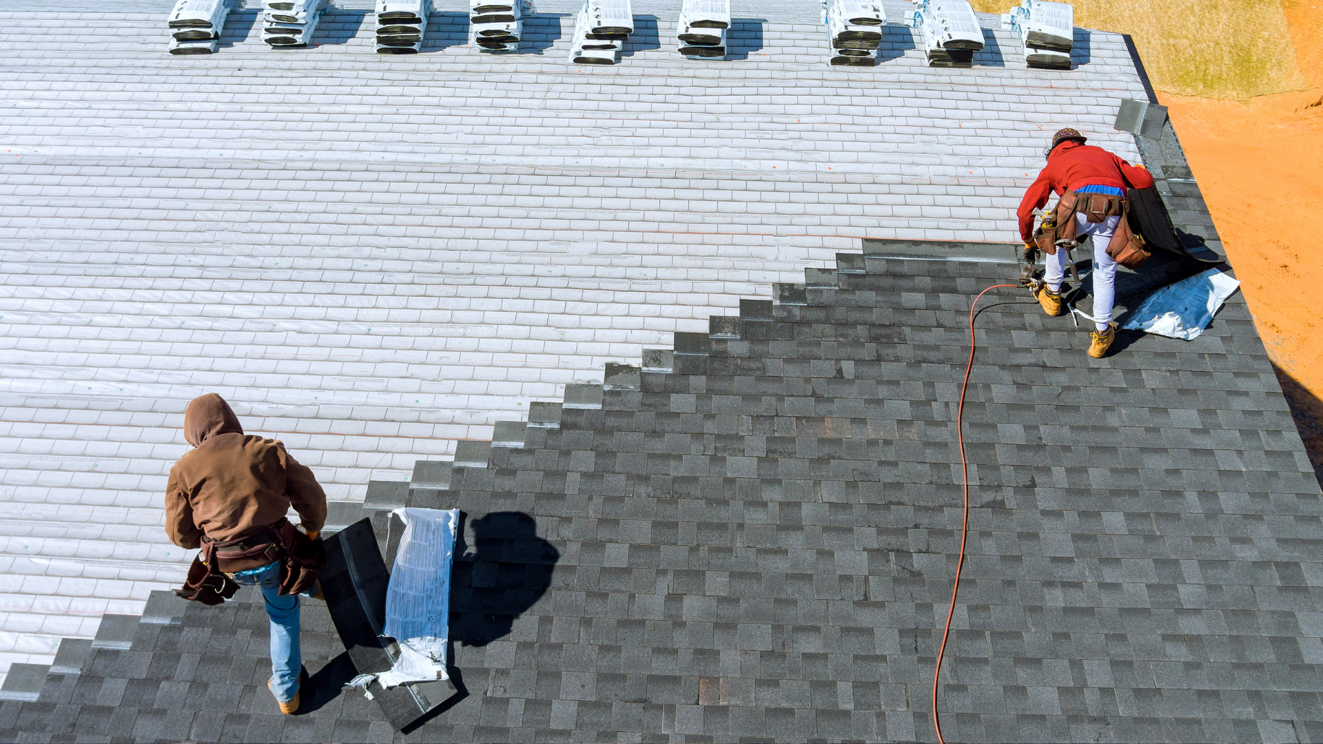 Two workers roofing a house, installing shingles on a sloped roof.