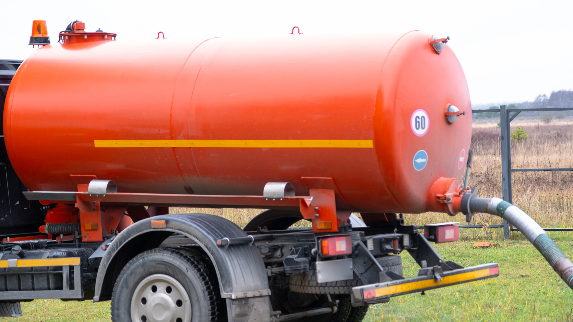 Orange water tanker trailer with hose, parked in a field