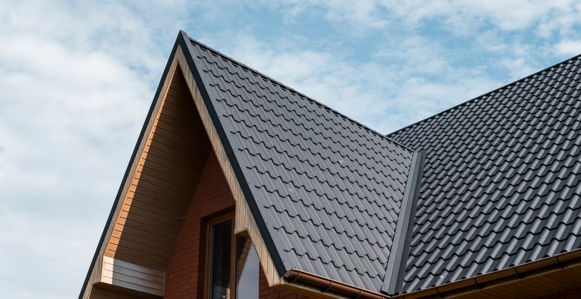 Close-up of a house roof with dark gray shingles against a blue sky