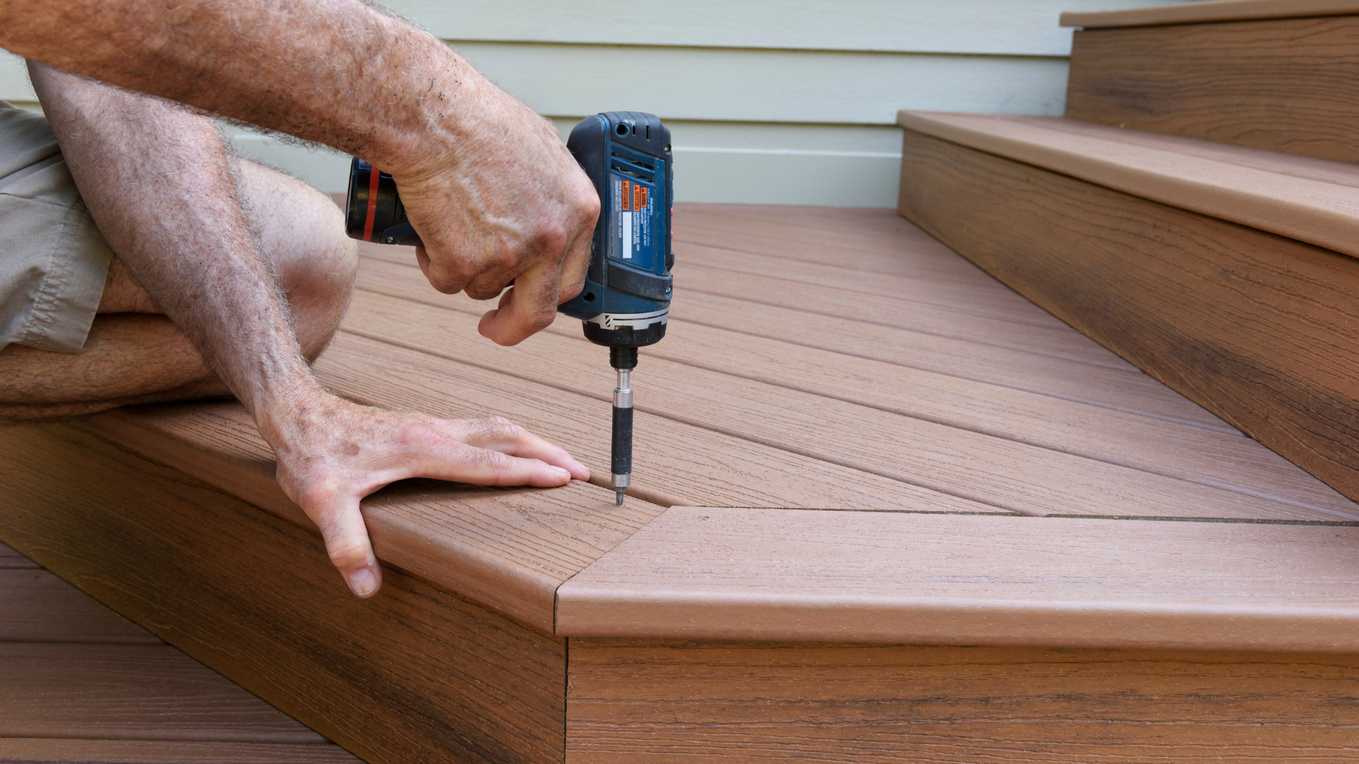 Person using a power drill to screw down composite deck boards on stairs.