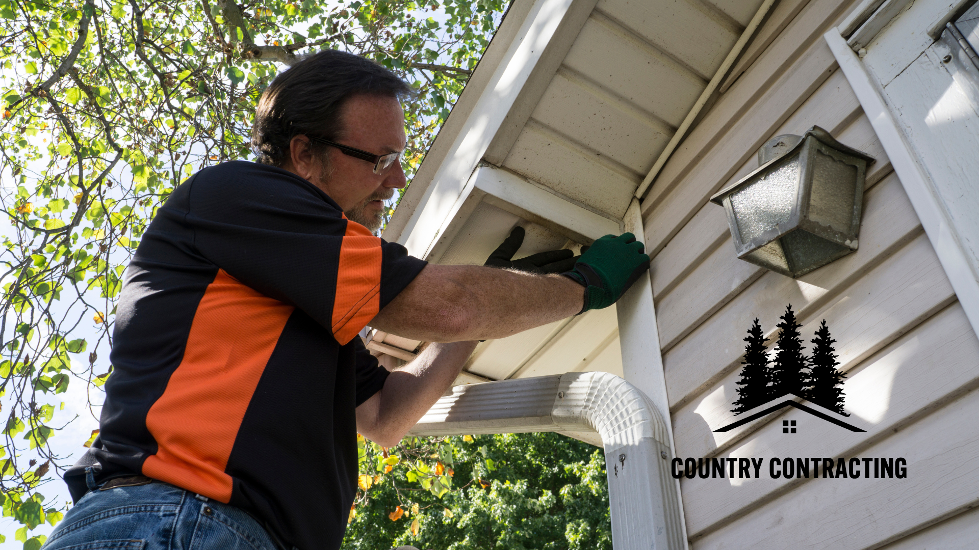 A man is working on the side of a house sponsored by country contracting