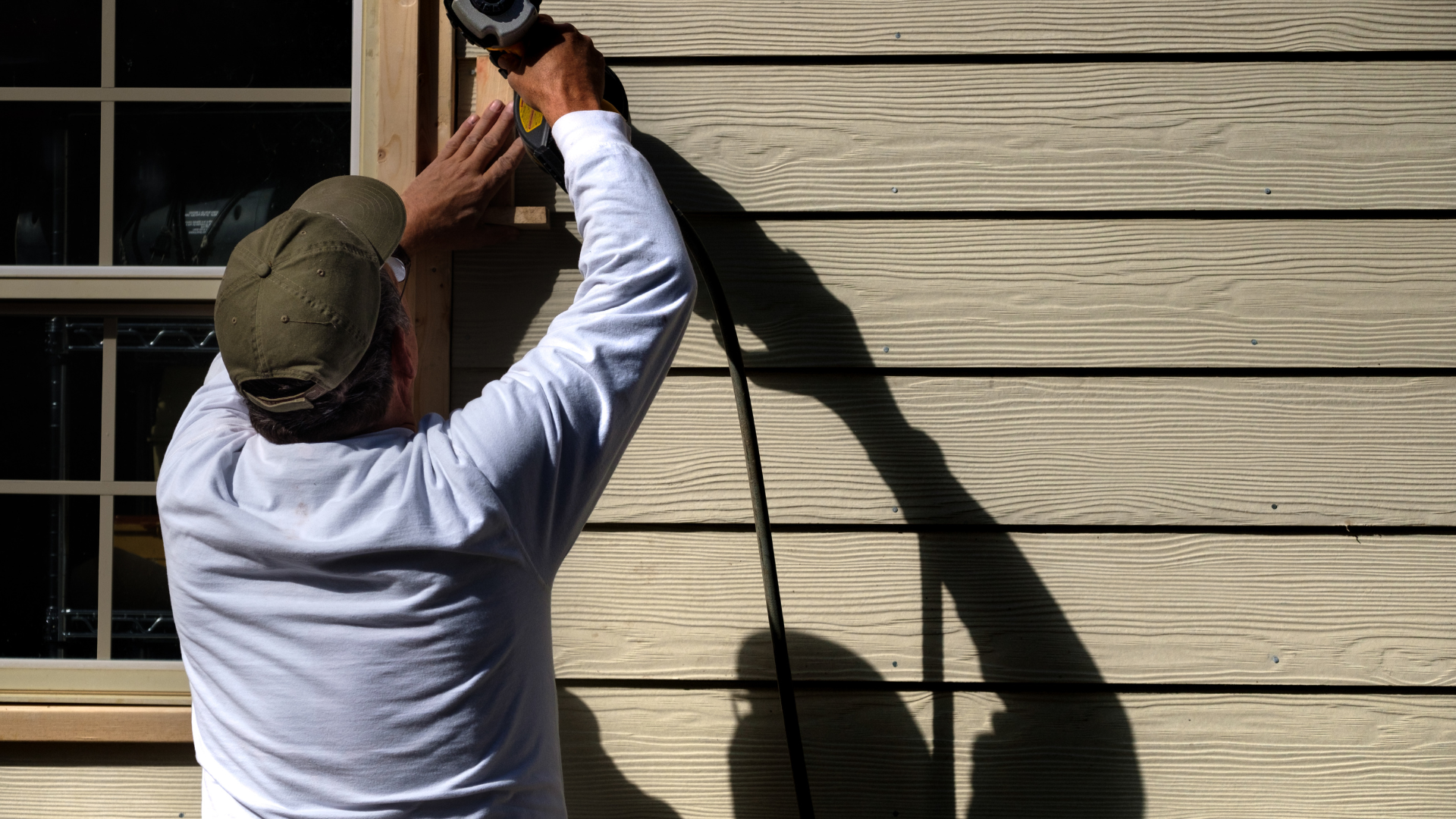 A man is working on a window frame on the side of a house.
