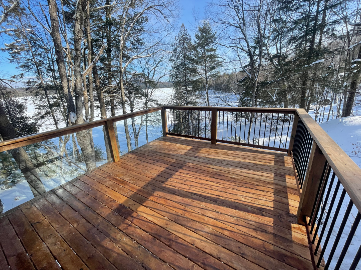 A wooden deck with a railing overlooking a snowy forest.