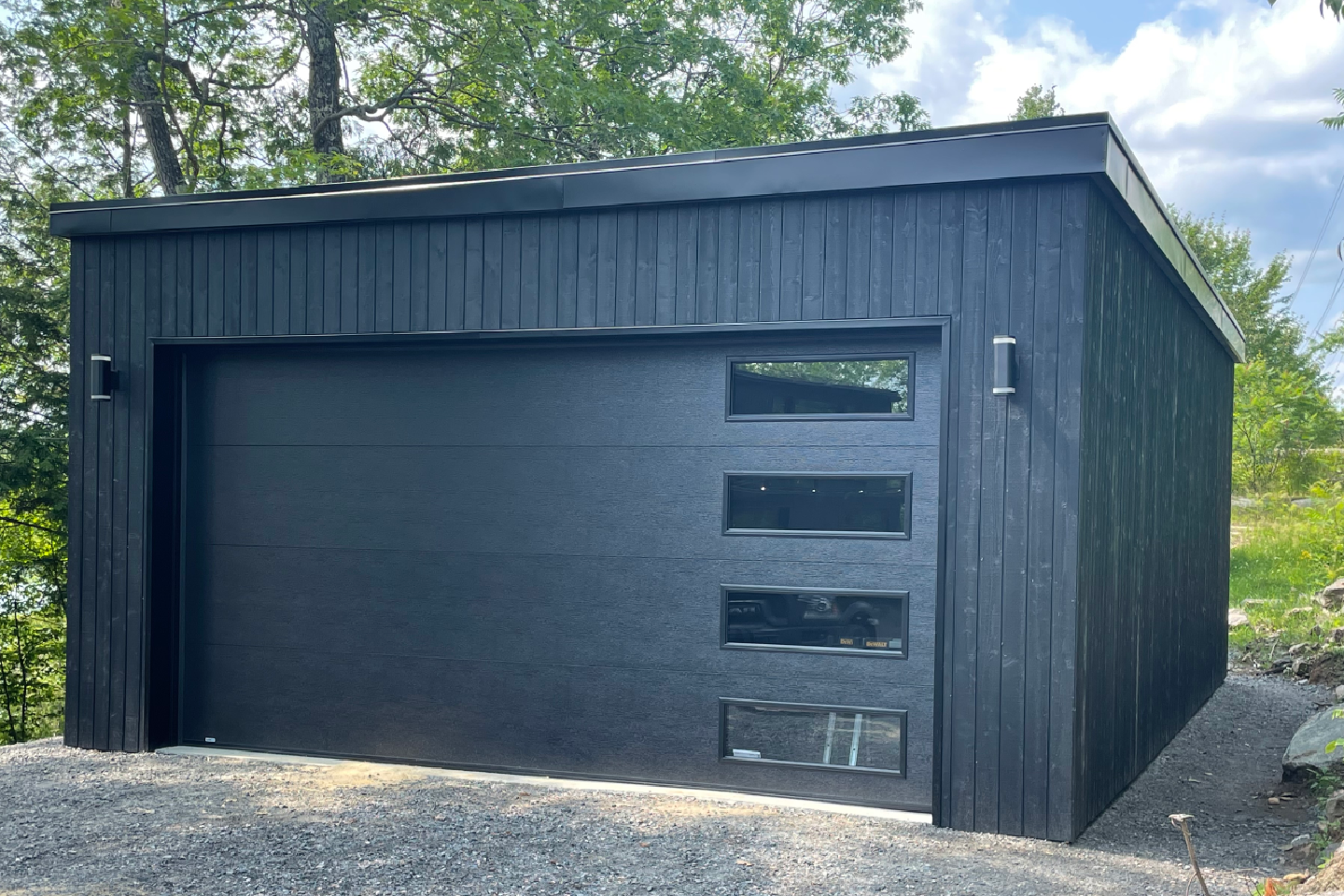 A black garage with a black door and windows is sitting on top of a gravel hill.