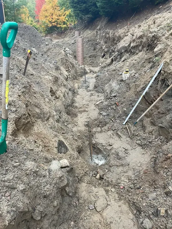 A shovel is sitting in the dirt next to a rake.