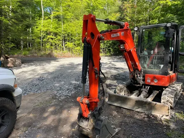 A small red excavator is parked next to a white truck.