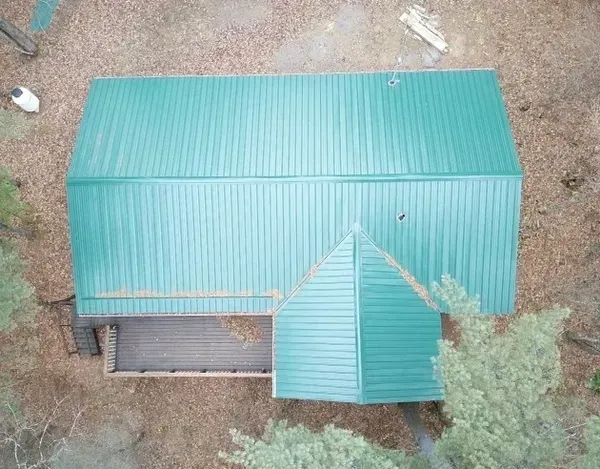 An aerial view of a green metal roof on a house in the woods.