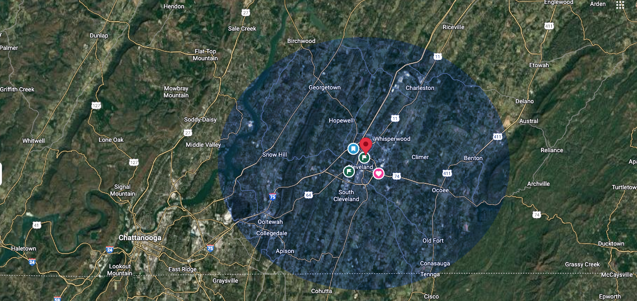 Aerial view of a city center, marked by a red pin, within a blue circle. Surrounding areas are green and rural.