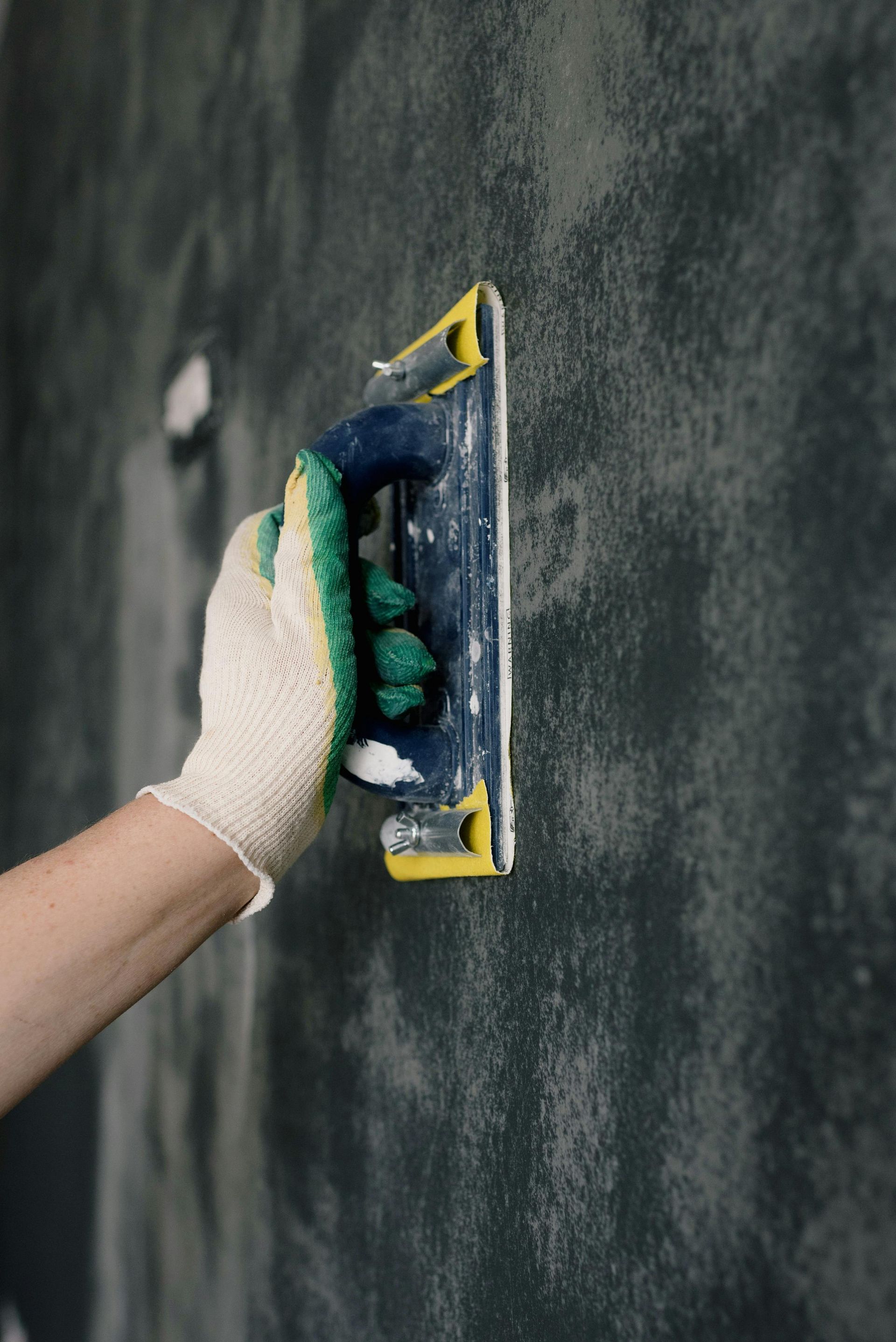 Hand sanding a dark wall with a sanding block and wearing a glove.