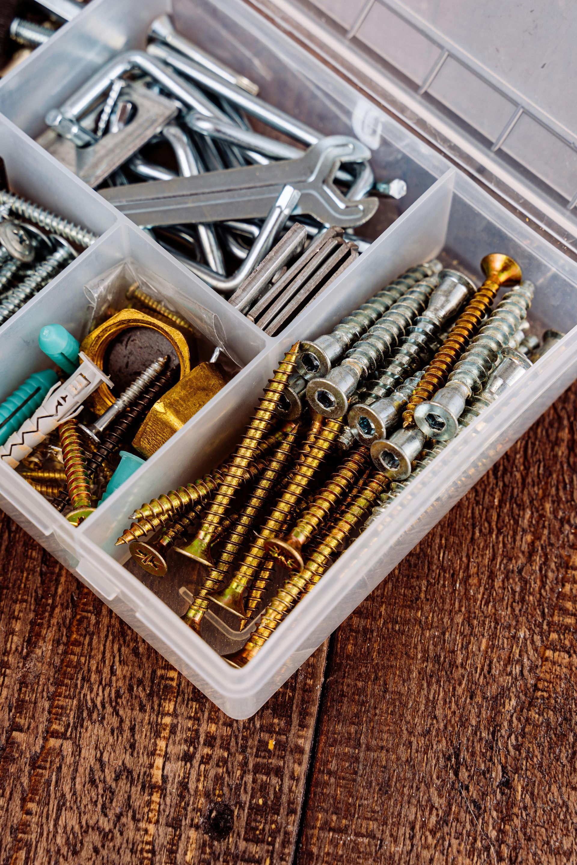 Open toolbox filled with screws, hooks, and wrenches on a wooden surface.