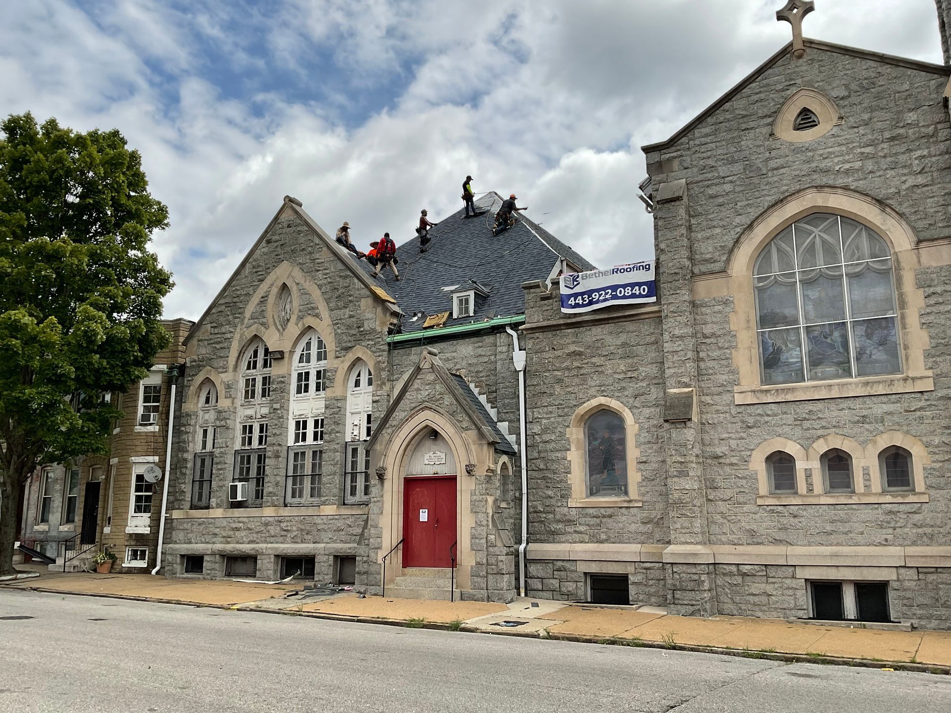 Church building with stone facade. Roofers working on roof under cloudy sky.