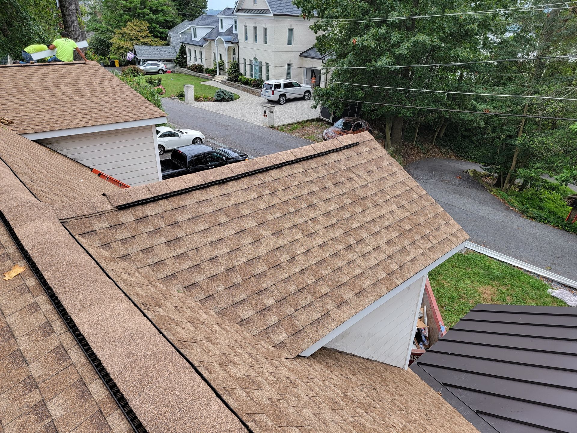 A brown shingled roof with workers, a street, and houses.