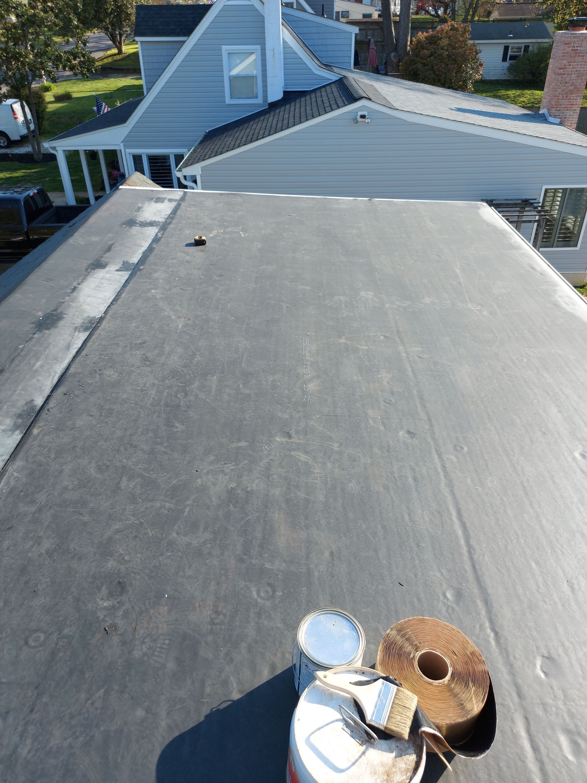 Black flat roof with repair materials, house in the background.