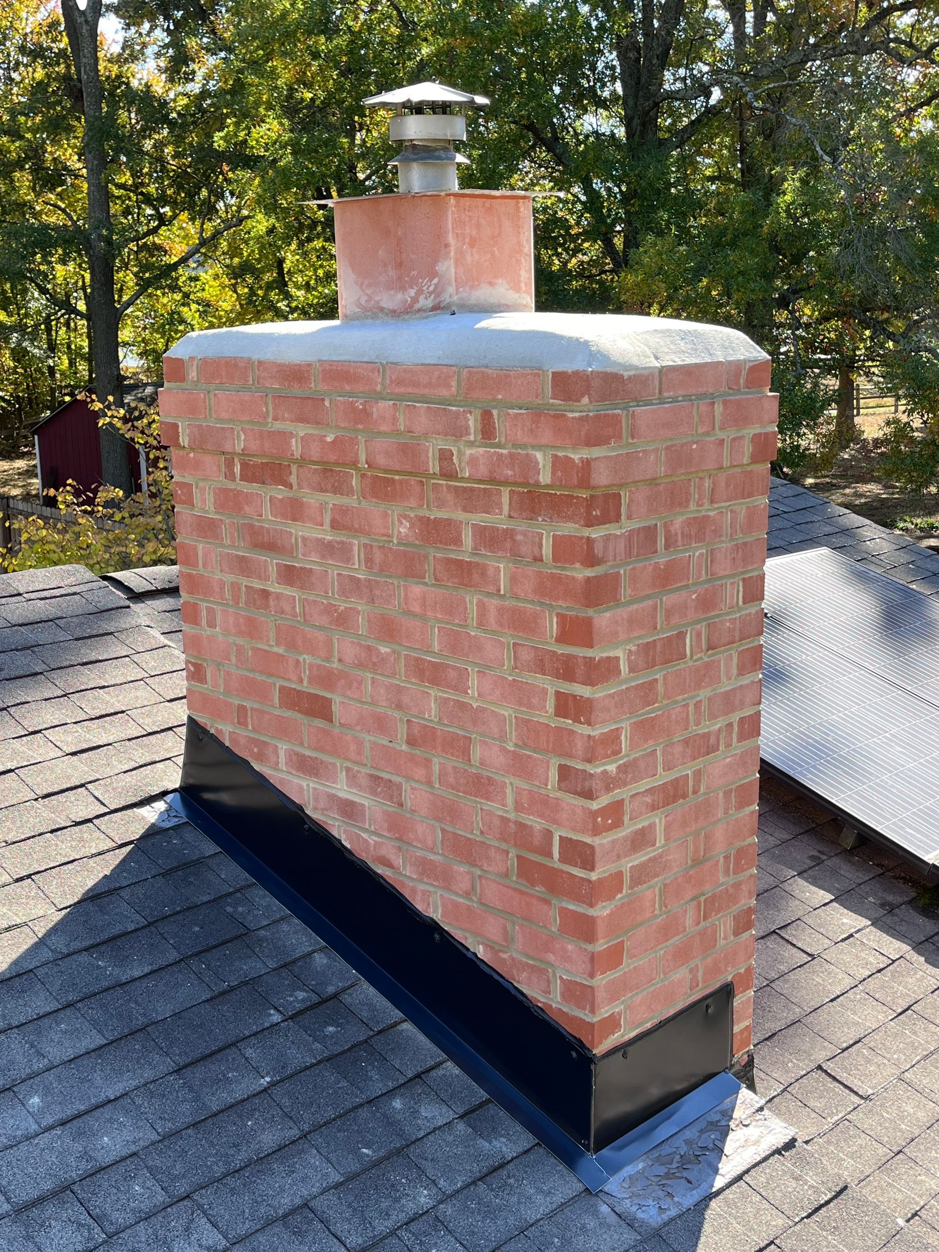 A man is working on a chimney on the roof of a house.