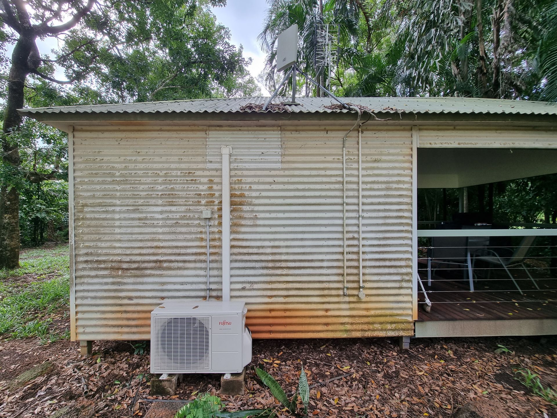 Weathered corrugated metal shed with air conditioner, antenna, and open porch in a wooded area — Prestige Painting NT in Zuccoli, NT