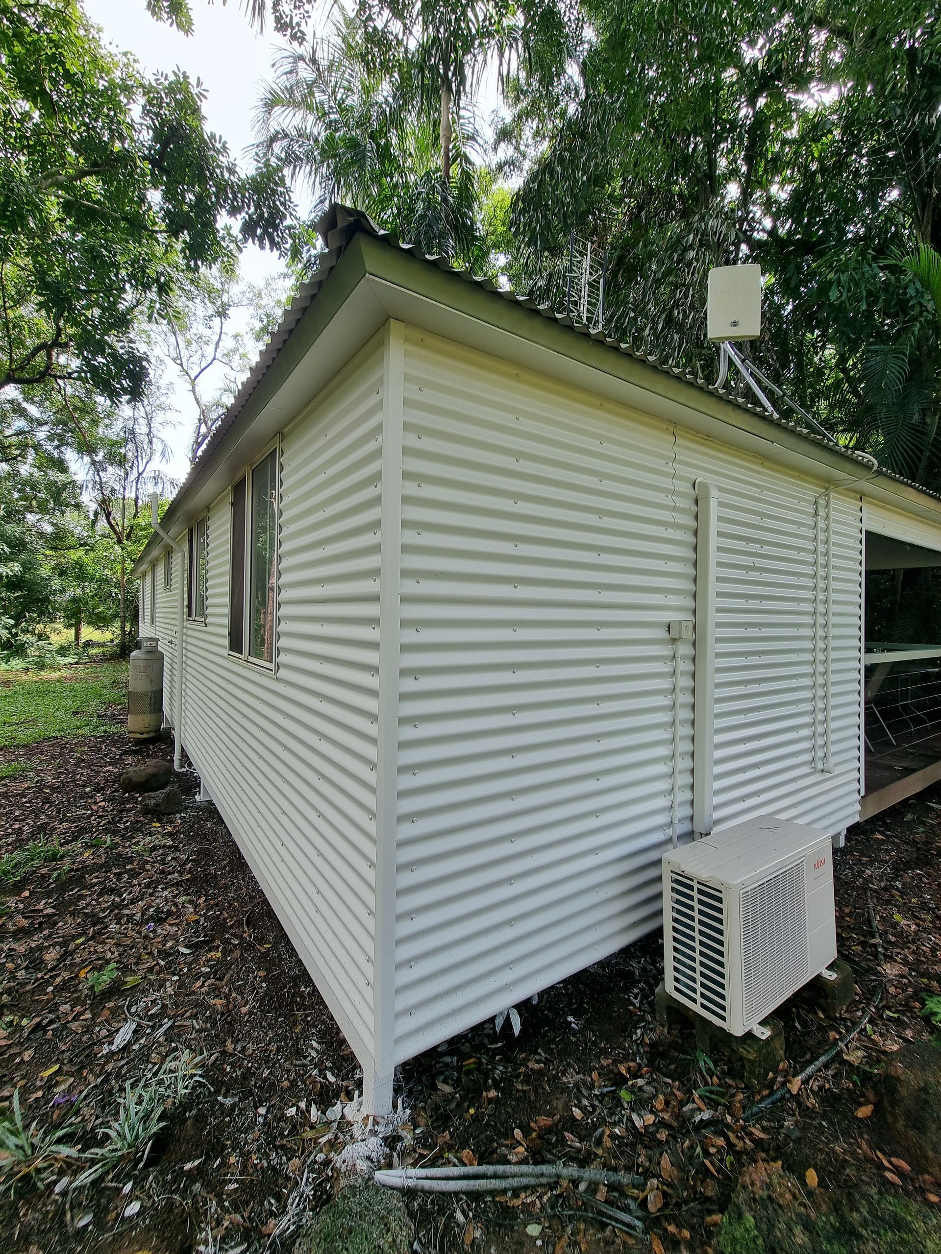 White corrugated metal building in a leafy outdoor setting; air conditioning unit visible — Prestige Painting NT in Zuccoli, NT