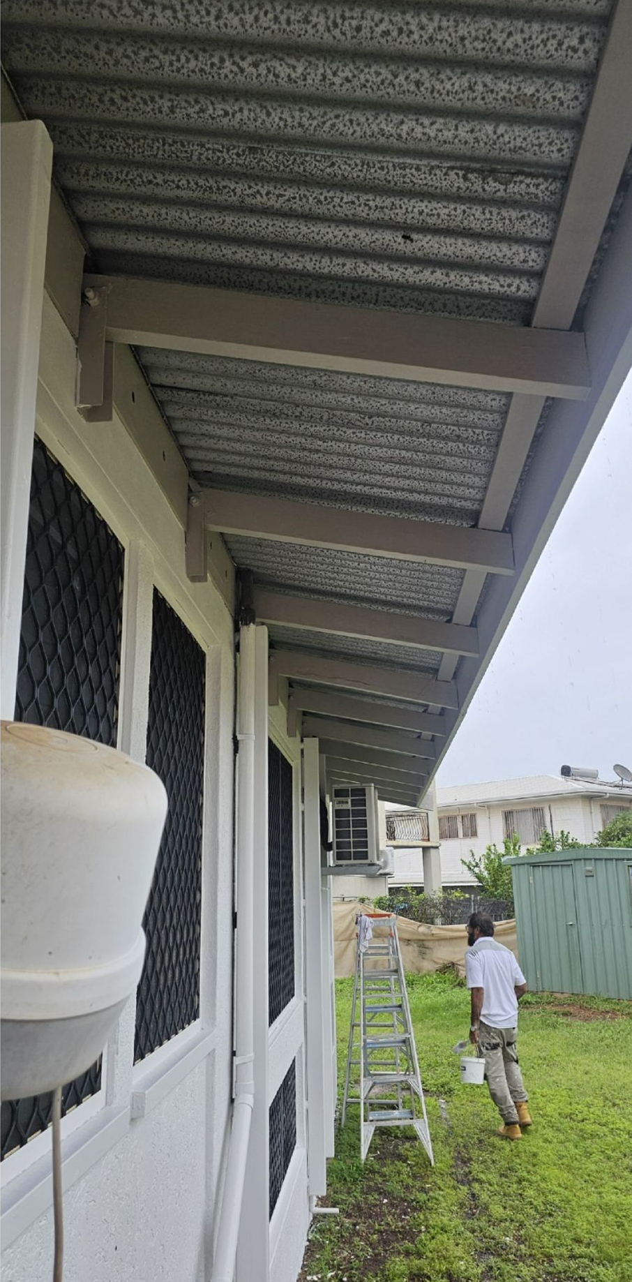 White building with a shaded veranda. A person on the lawn near a ladder is working on the house — Prestige Painting NT in Zuccoli, NT