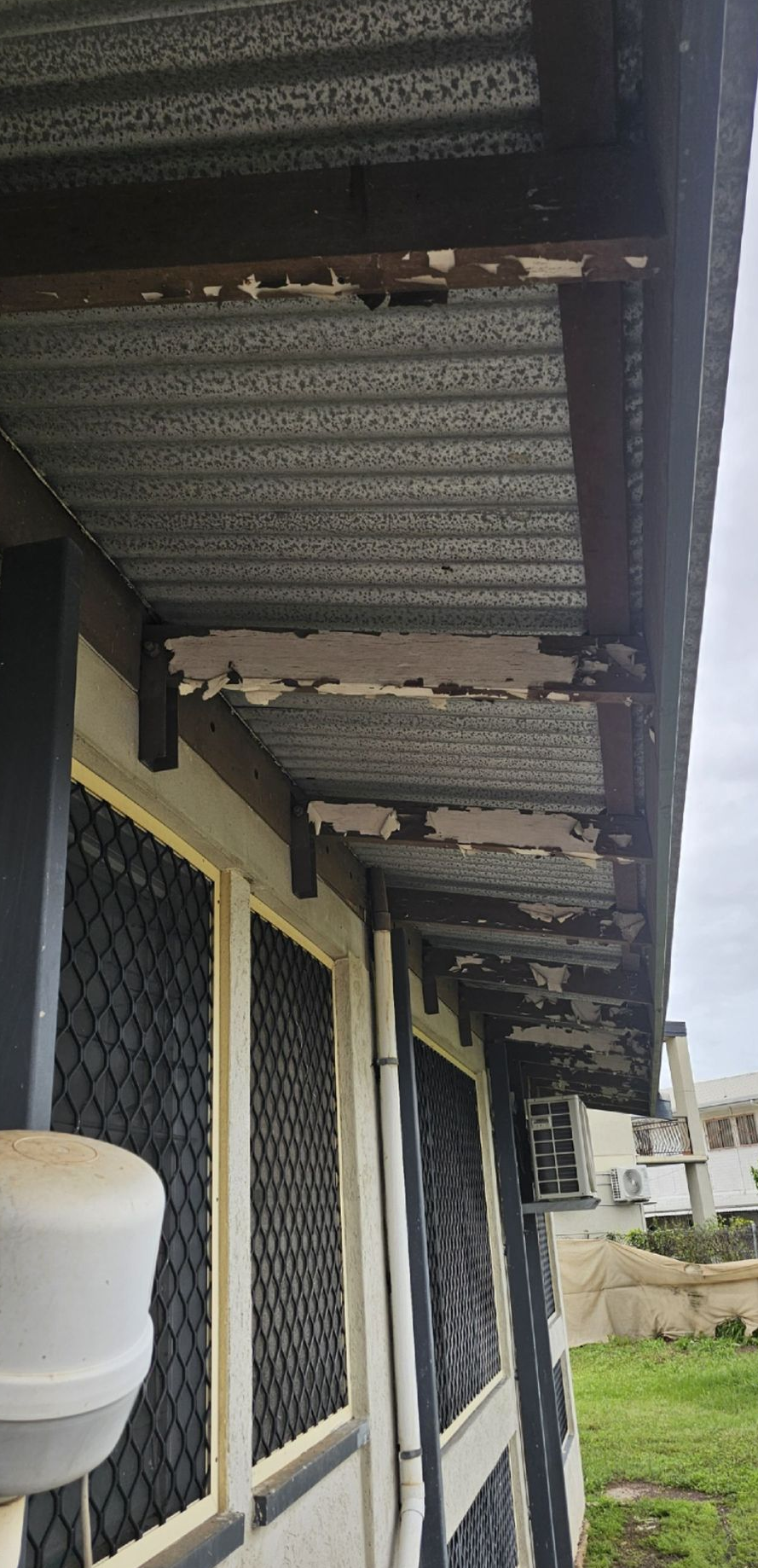Close-up of a building's roof with peeling paint and metal panels. Windows with screens are visible — Prestige Painting NT in Zuccoli, NT