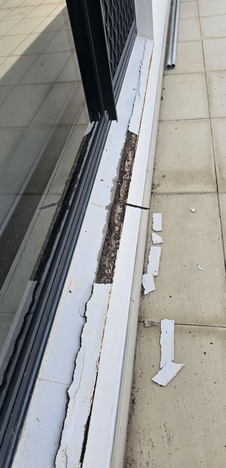 Damaged window sill with peeling white paint, debris, and a dark metal grate. Exterior shot — Prestige Painting NT in Zuccoli, NT