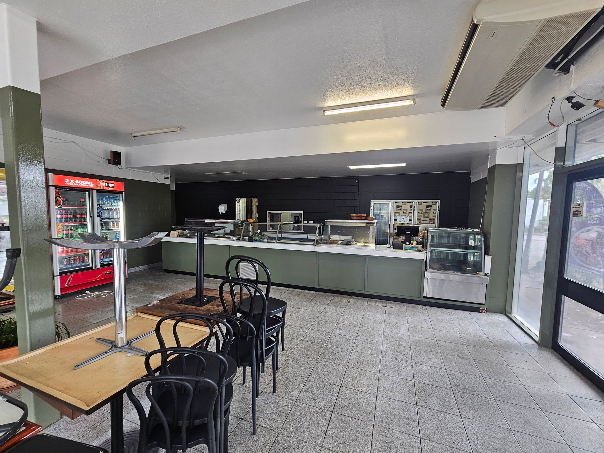 Empty cafeteria interior with tables, chairs, food service counters, refrigerator, and exterior door — Prestige Painting NT in Zuccoli, NT