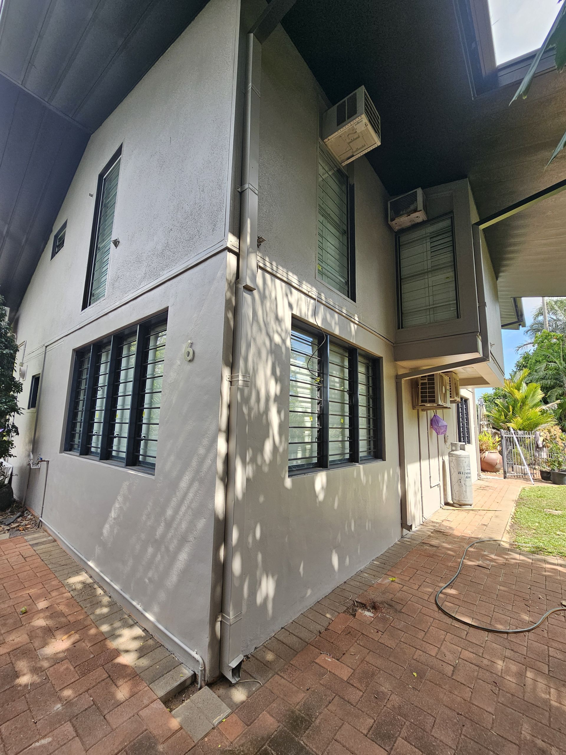Two-story building with light-coloured stucco walls, black-framed windows, and air conditioning units — Prestige Painting NT in Zuccoli, NT