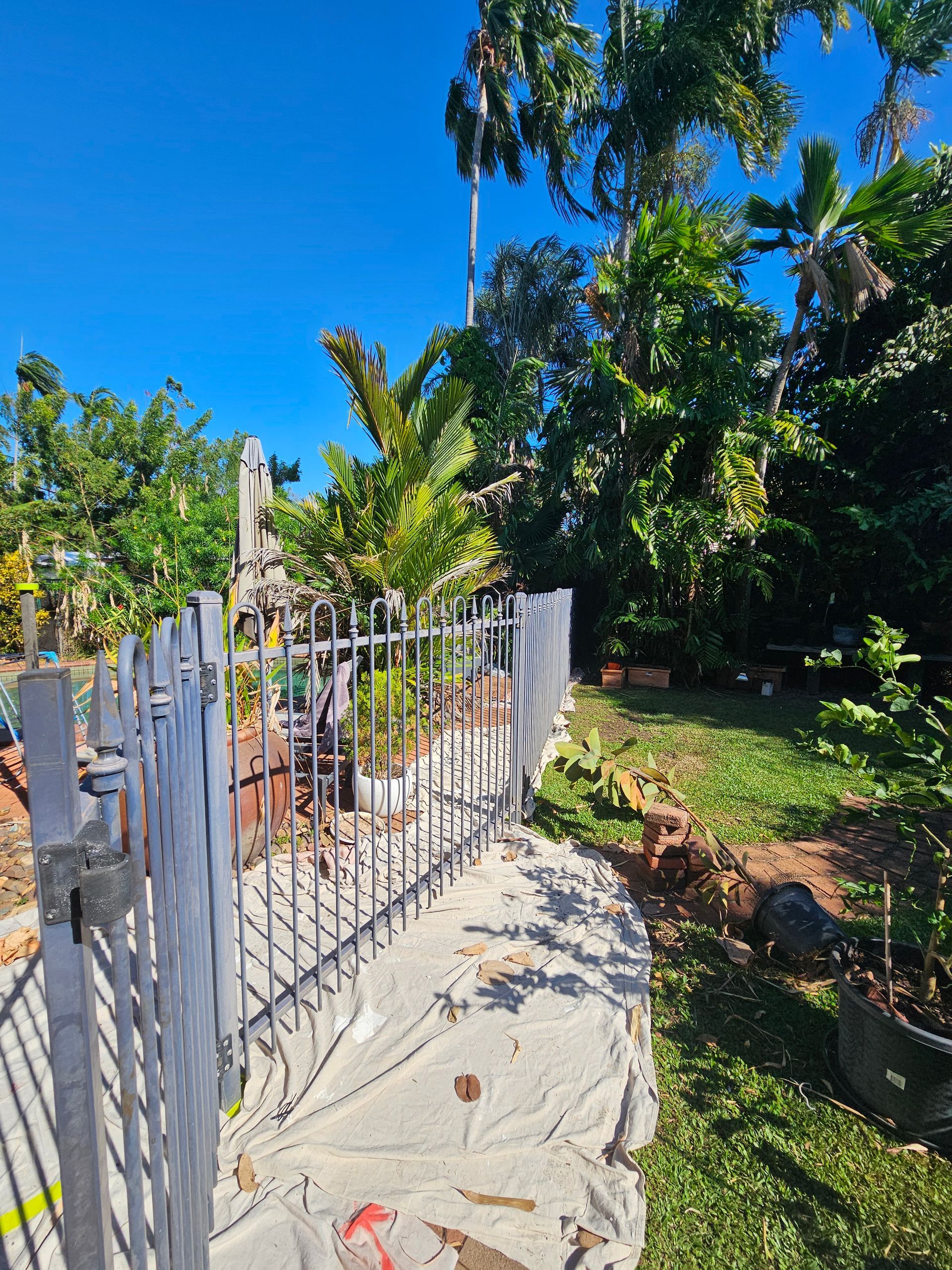 A metal gate opens to a garden with green foliage, a concrete border, and a bright blue sky — Prestige Painting NT in Zuccoli, NT