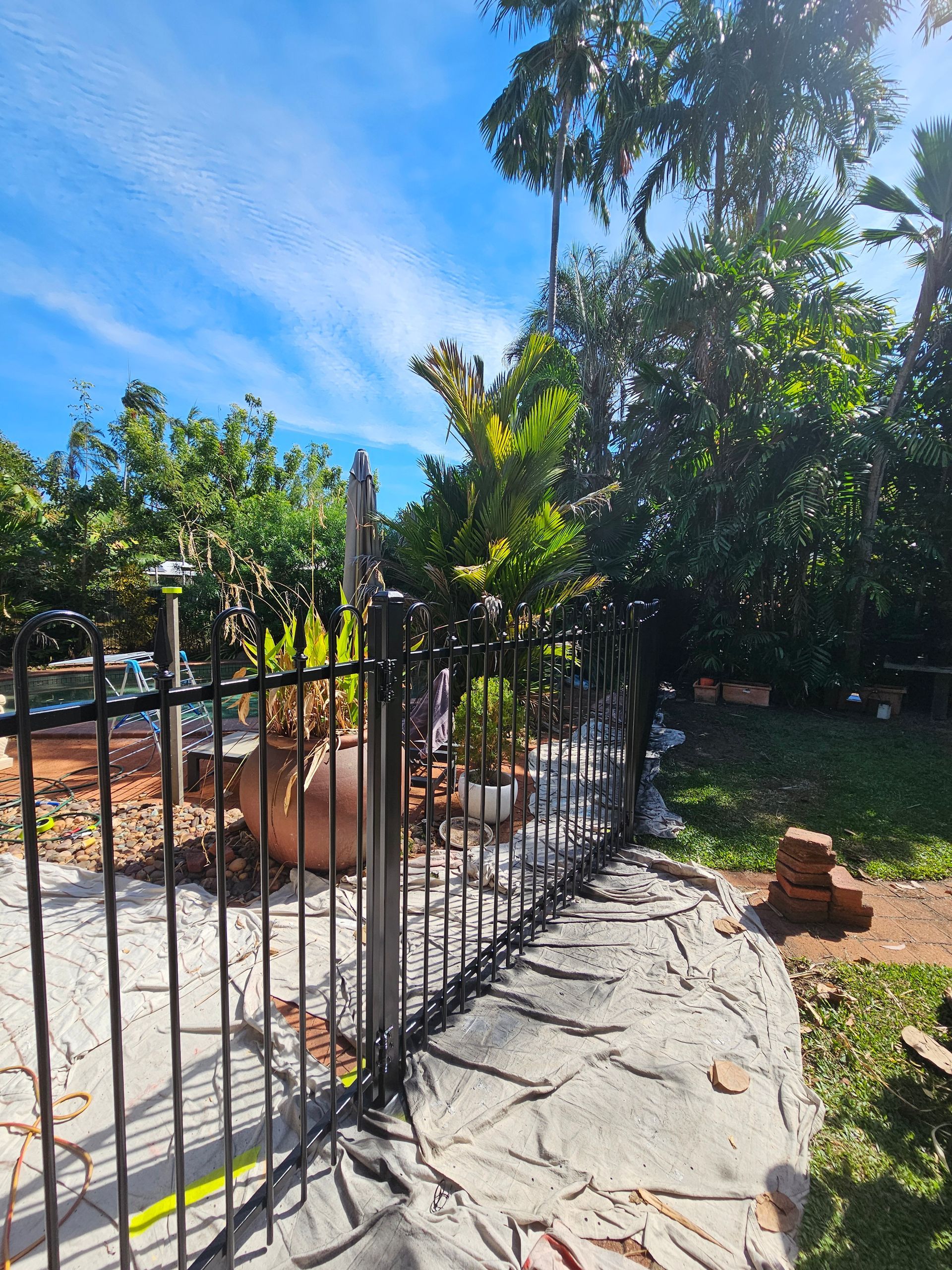 Black metal fence along a stone wall, trees, and blue sky — Prestige Painting NT in Zuccoli, NT