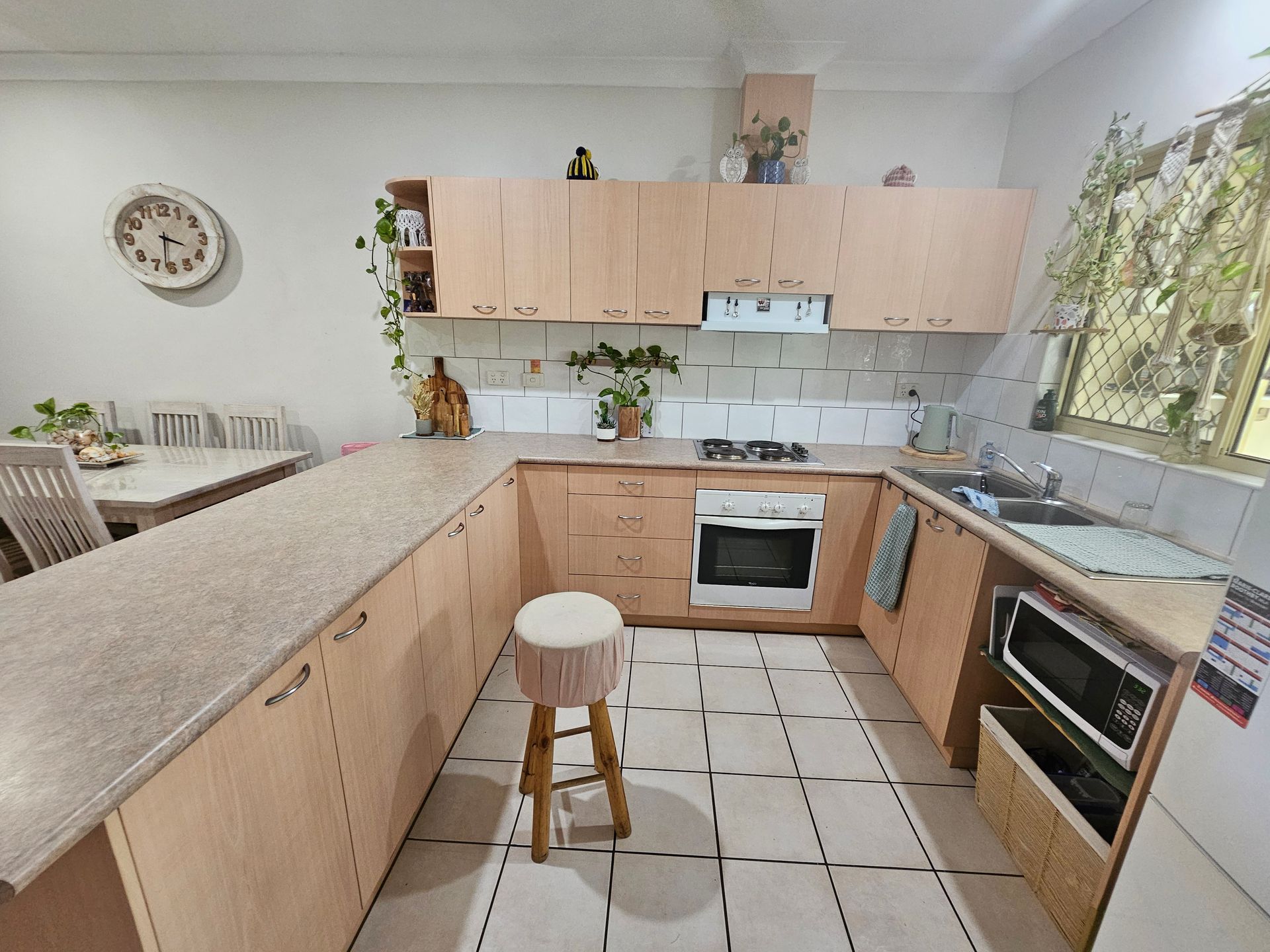 Beige kitchen with countertops, cabinets, stove, sink, and a microwave. A wooden stool sits in the middle — Prestige Painting NT in Zuccoli, NT