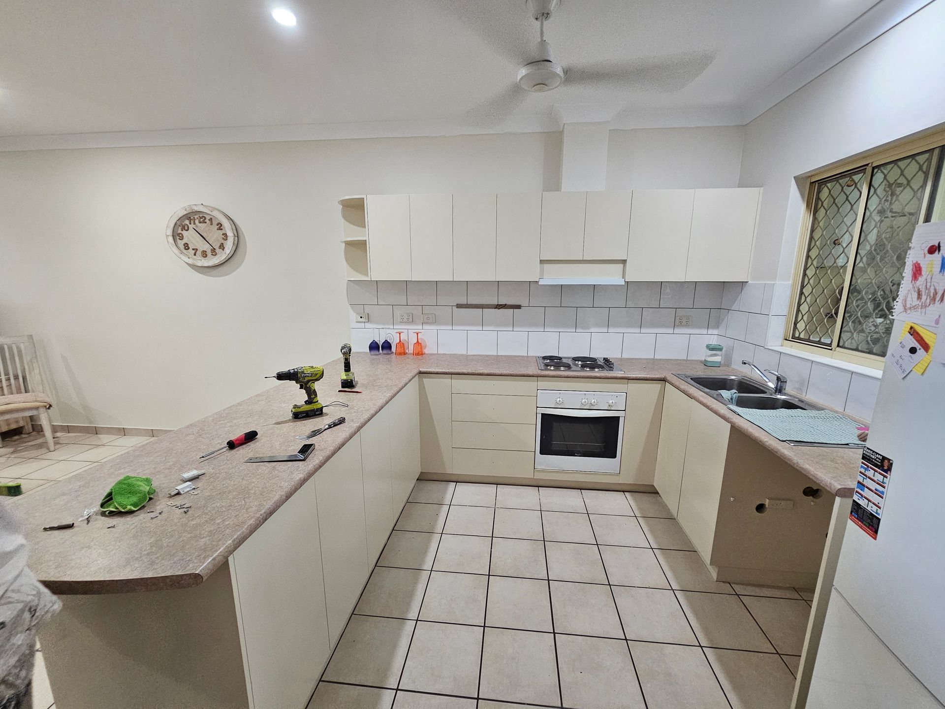 A U-shaped kitchen with cream cabinets, oven, and countertop. A drill lies on the countertop — Prestige Painting NT in Zuccoli, NT