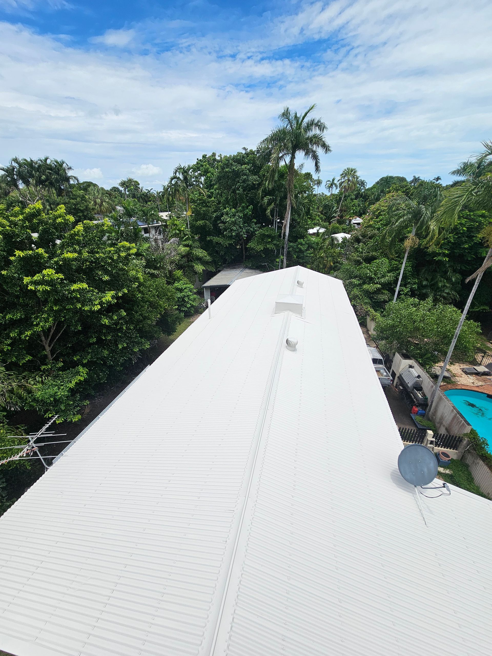 White roof with a satellite dish, surrounded by lush green trees under a blue sky — Prestige Painting NT in Zuccoli, NT