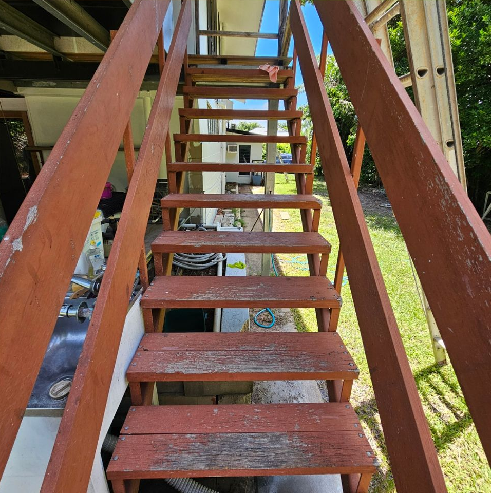 Wooden outdoor stairs with red-painted railings lead upwards. Weathered steps on a sunny day — Prestige Painting NT in Zuccoli, NT