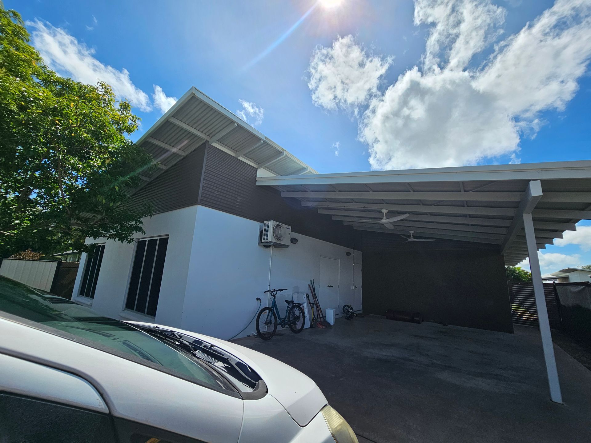 White house with brown siding, carport, two bikes, and blue sky with clouds — Prestige Painting NT in Zuccoli, NT