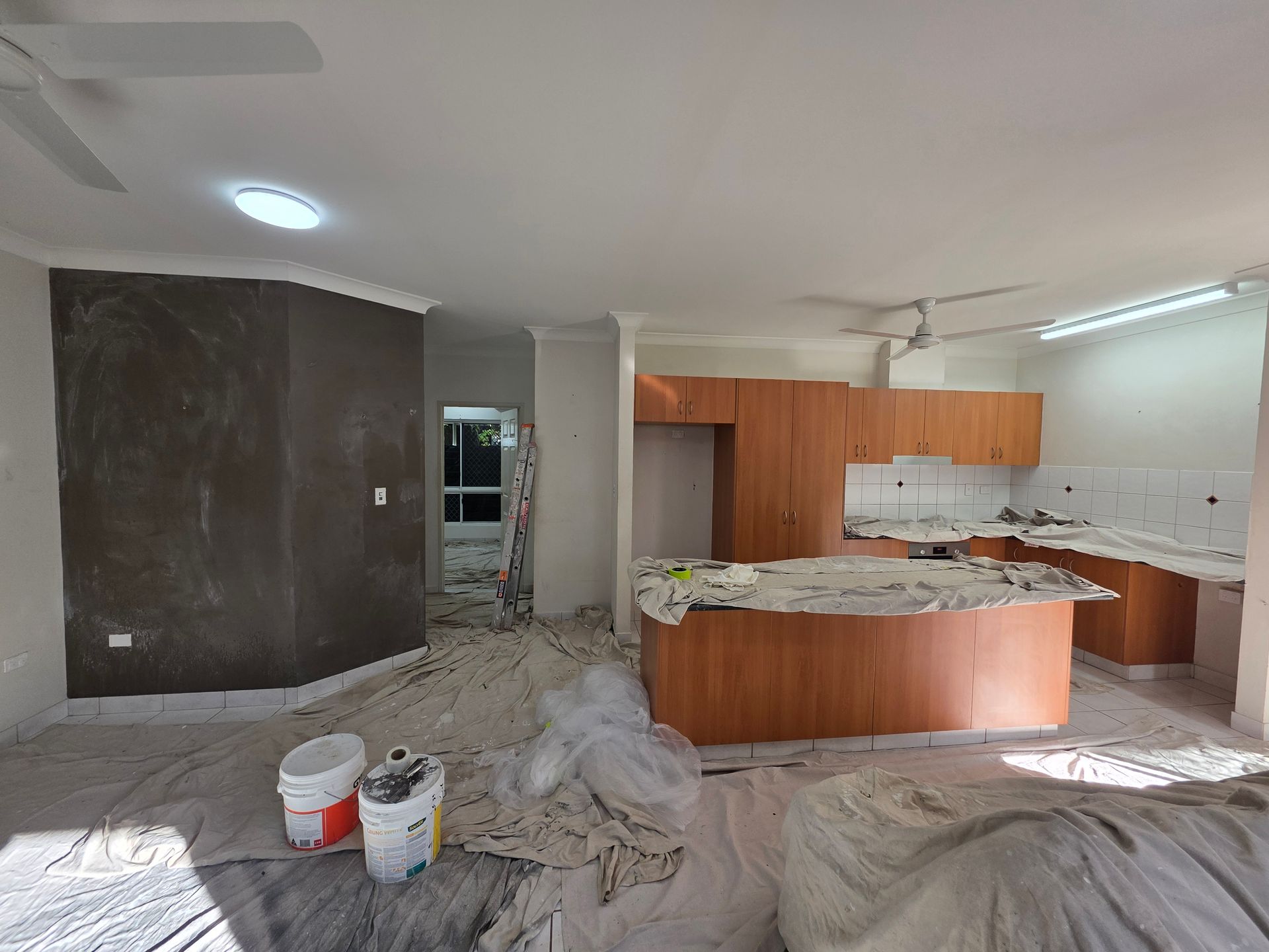 Interior renovation: kitchen and entryway, brown cabinetry, gray and white walls, paint supplies on floor — Prestige Painting NT in Zuccoli, NT