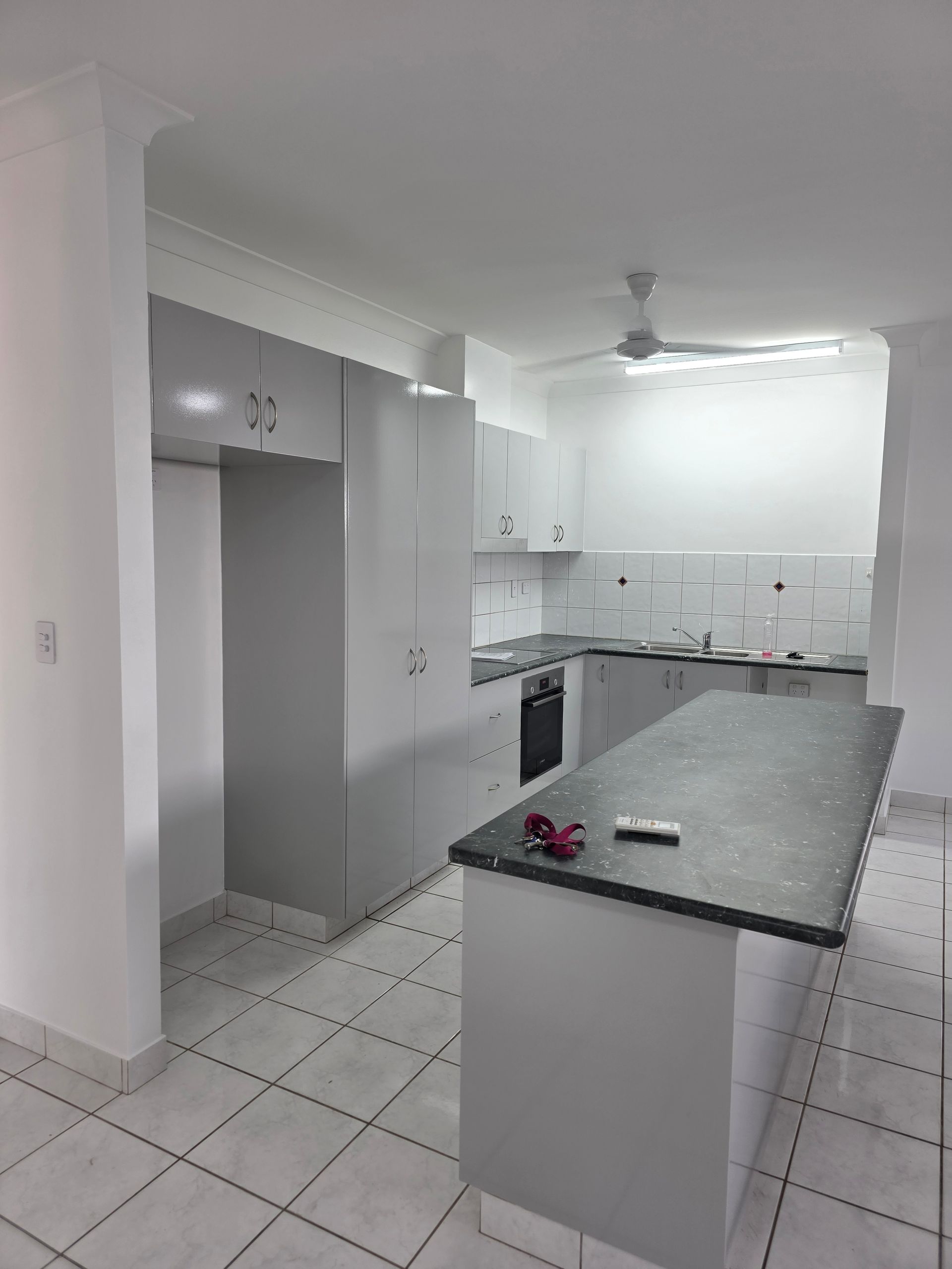 A modern kitchen with grey cabinets, a dark countertop island, and white tiled floor — Prestige Painting NT in Zuccoli, NT