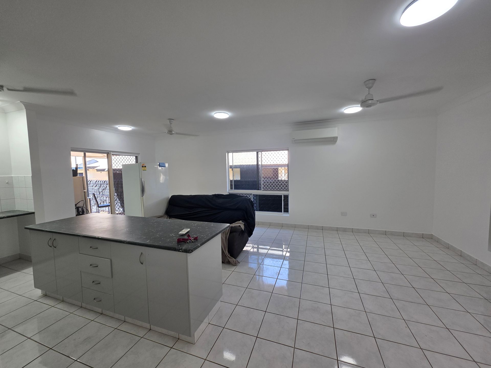 Open-plan living space with kitchen island, tiled floor, white walls, and a sofa near windows — Prestige Painting NT in Zuccoli, NT