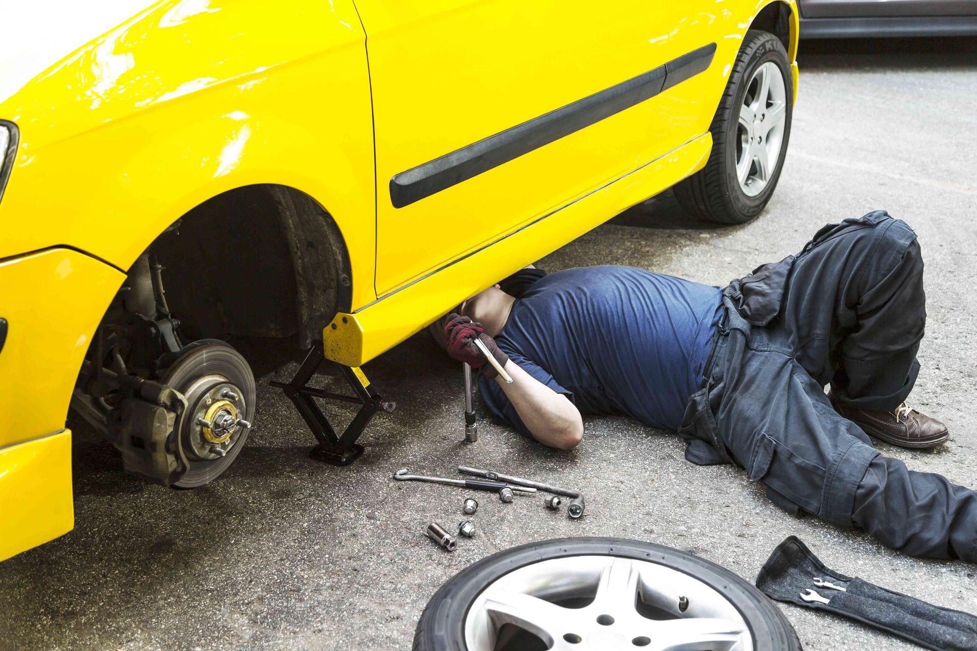 a man laying on the ground working on a yellow car