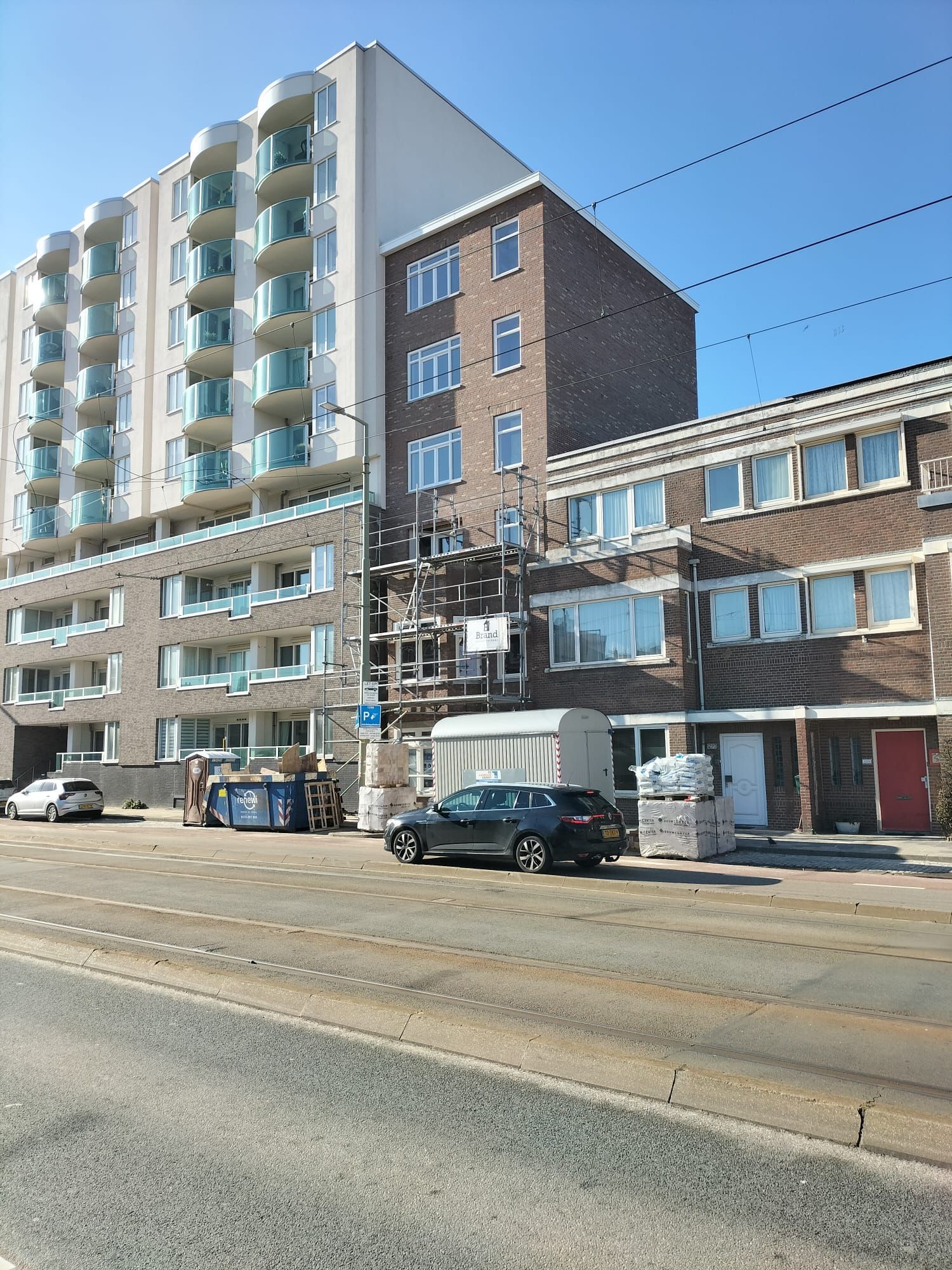 Gebouwen in een stadsstraat; een hoog appartementencomplex, een bakstenen gebouw met steigers en een rij rijtjeshuizen.