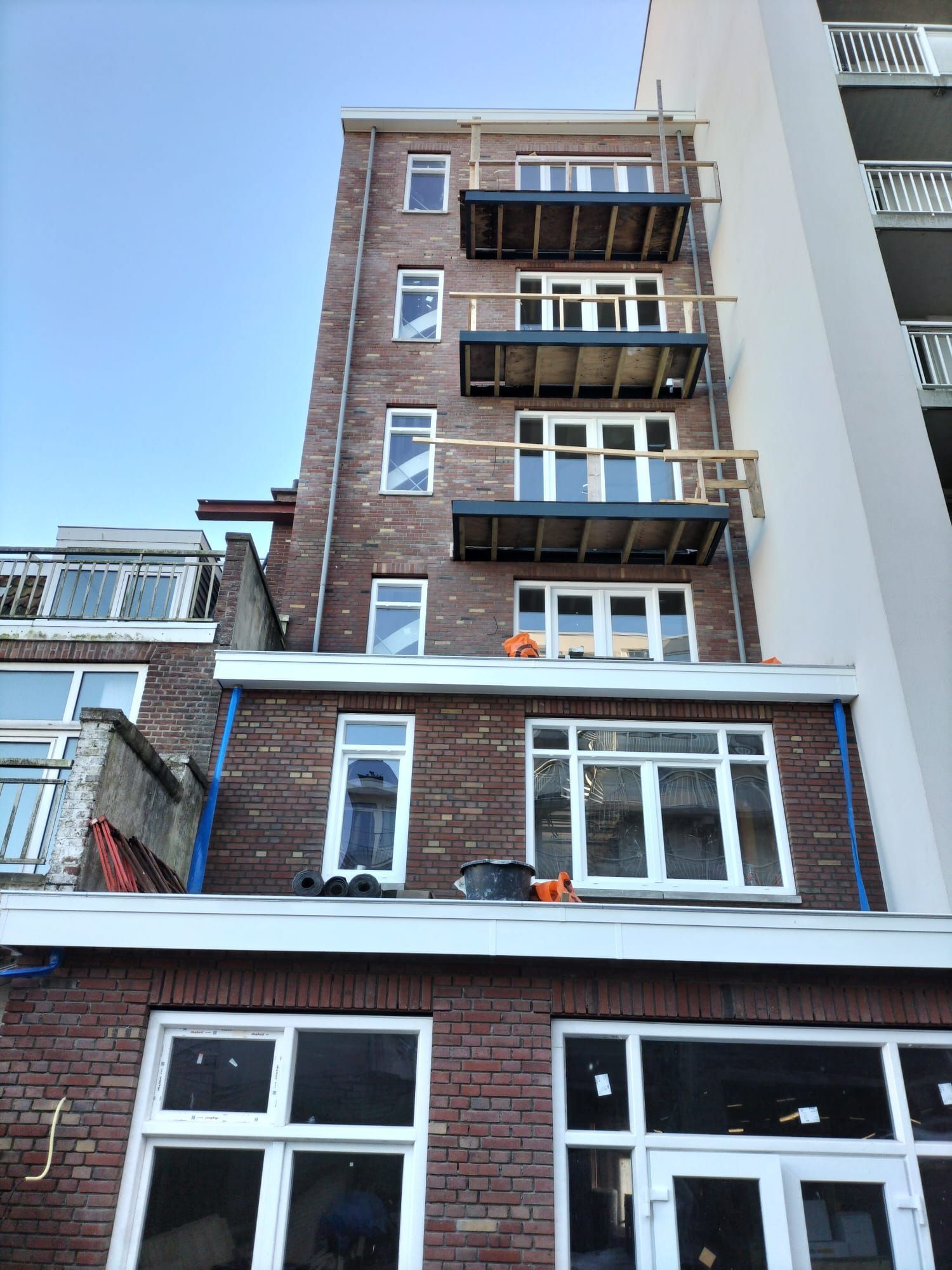 Bakstenen gebouw met balkons in aanbouw; blauwe lucht.