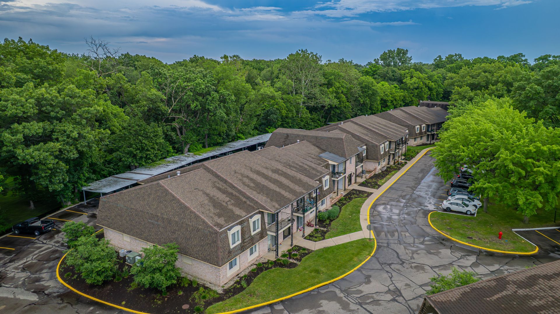 Aerial view of apartment complex with brown roofs surrounded by green trees.