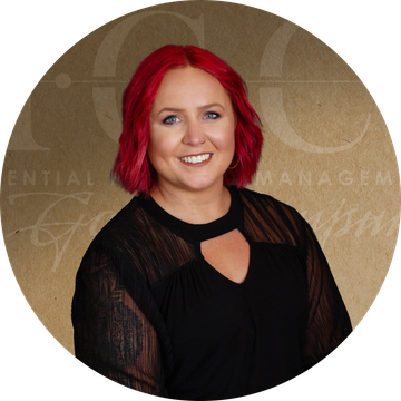 Woman with red hair smiling, wearing a black shirt with a keyhole neckline, in front of a golden background with a logo.