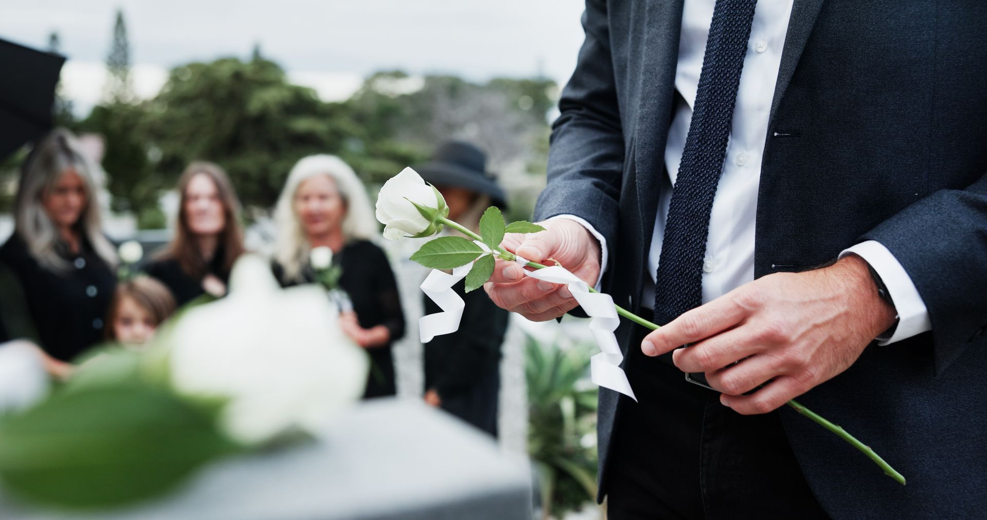 A group of people in formal attire carrying a wooden casket topped with white flowers down stone steps at a funeral.