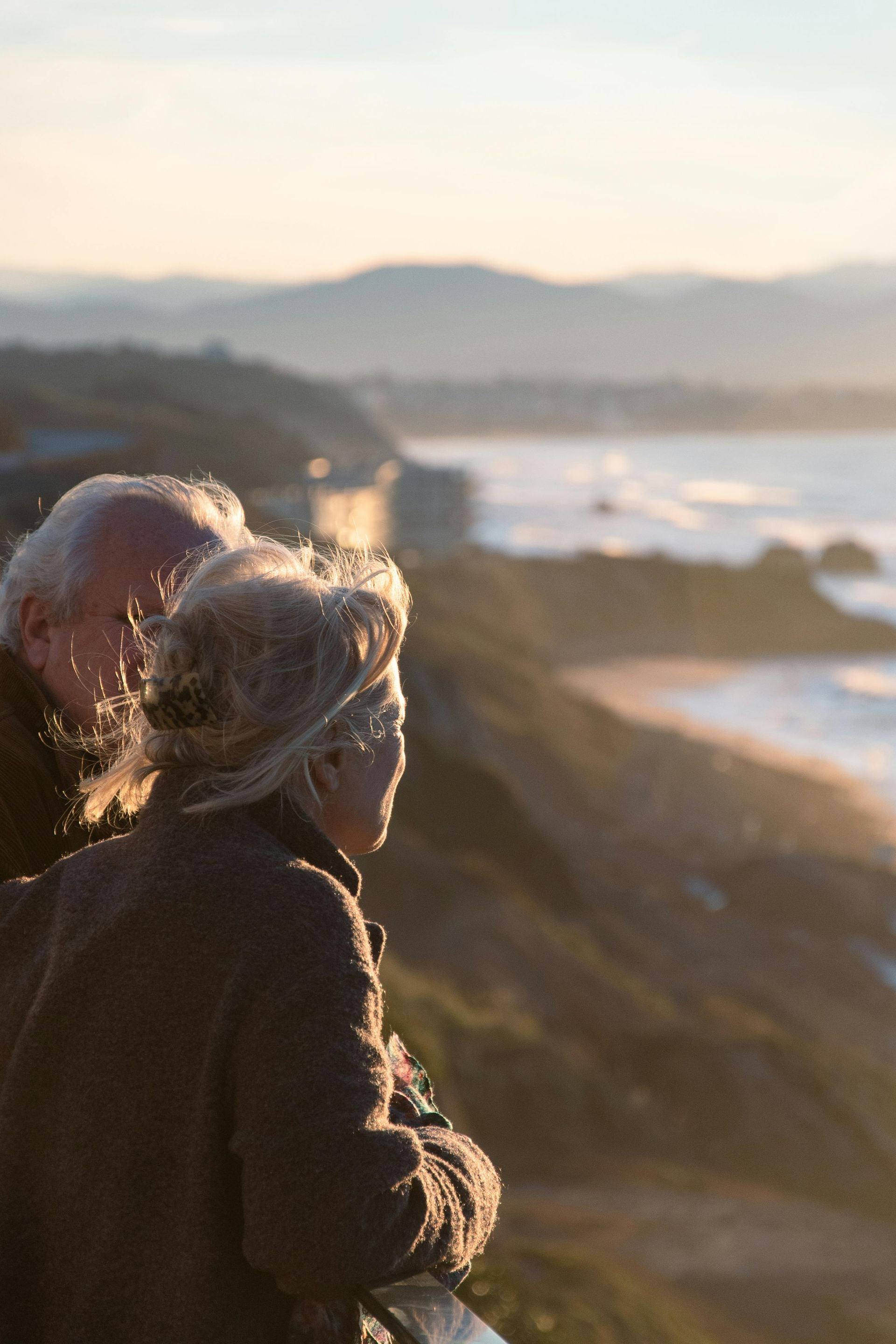 Two people in coats looking over a rocky coastline at sunset