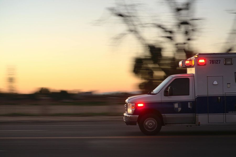 Ambulance with flashing lights speeding along a road at dusk