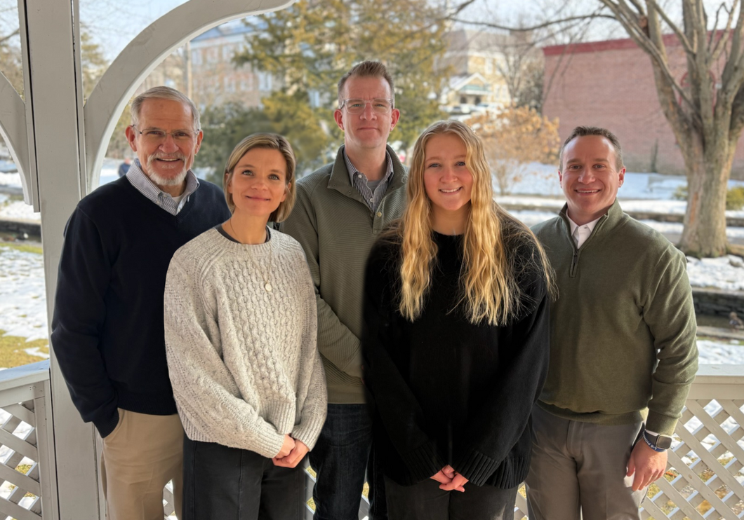 Five people stand together in a gazebo, smiling for a group portrait on a sunny day.