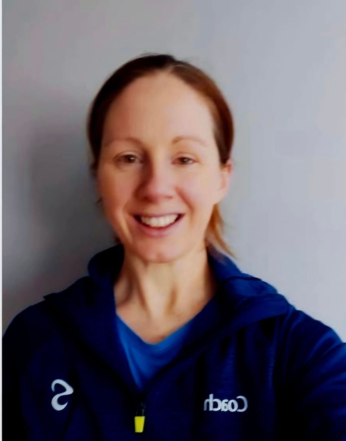 Smiling person in a blue jacket and shirt against a plain light background.