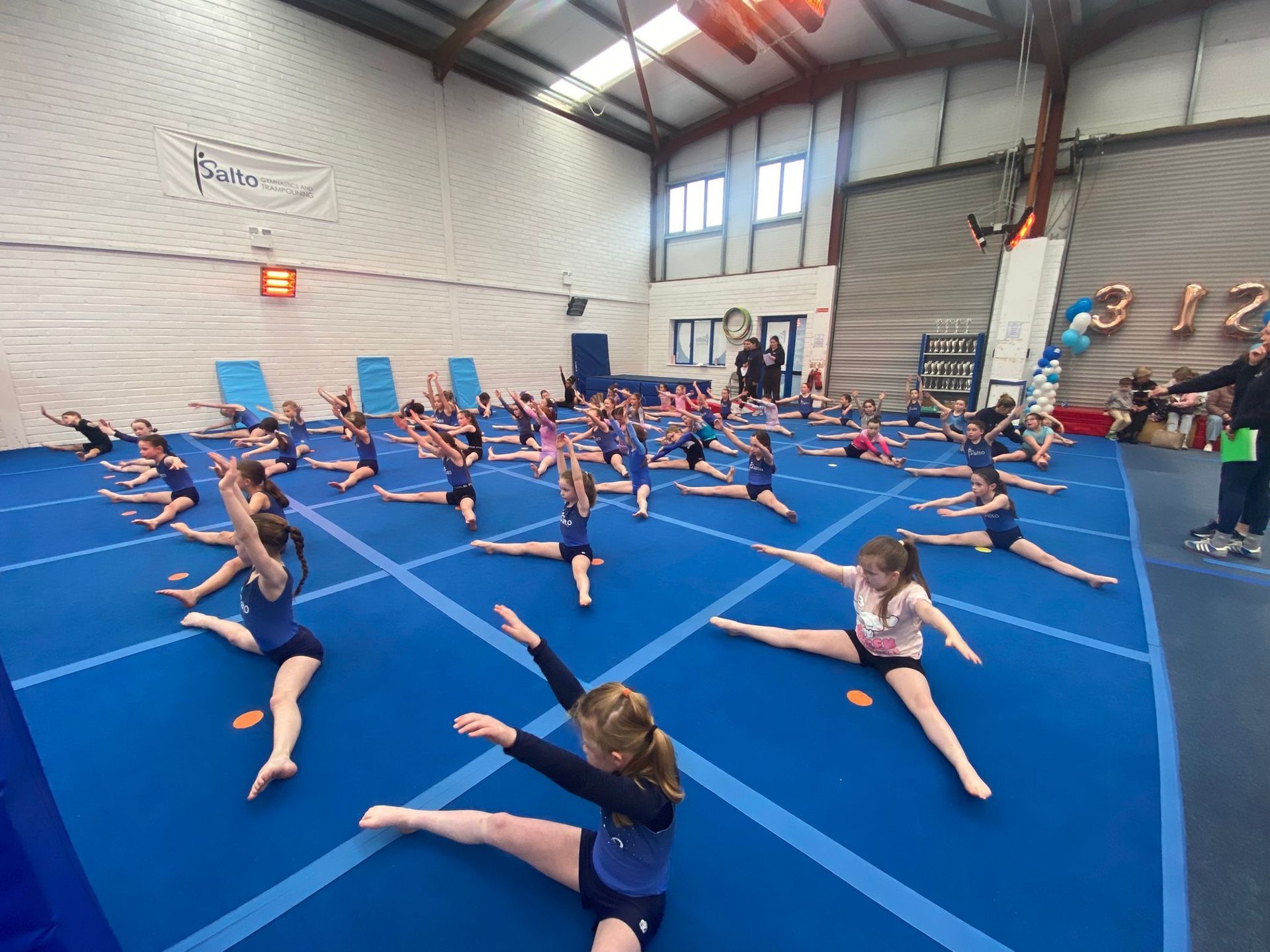 Gymnastics class stretching on blue mats in a gymnasium